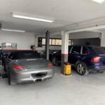 Γκρι Porsche και μπλε Porsche Cayenne παρκαρισμένα στο εσωτερικό του συνεργείου.